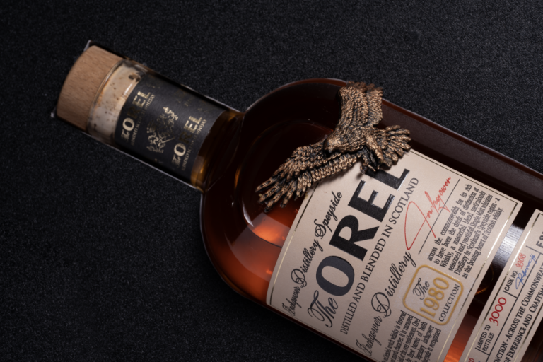 Ảnh cận chai whisky The OREL nằm nghiêng, tượng đại bàng đồng gắn trên vai chai, nút bần và nhãn Speyside, nền tối, thực hiện bởi Lus Photo