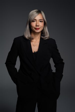 Chụp ảnh chân dung doanh nhân nữ tóc nhuộm bạc mặc suit đen phối áo ren đen, hai tay đút túi quần trên phông nền xám, thực hiện bởi Lus Photo