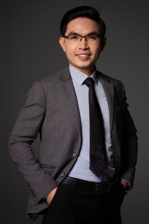 Chụp ảnh chân dung doanh nhân nam mặc vest xám thắt cà vạt sọc đen, tay đút túi quần trên phông nền xám, thực hiện bởi Lus Photo