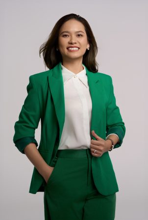 Chụp ảnh chân dung doanh nhân nữ tóc dài mặc vest xanh lá liền bộ phối sơ mi lụa trắng, một tay đút túi trên phông nền sáng, thực hiện bởi Lus Photo